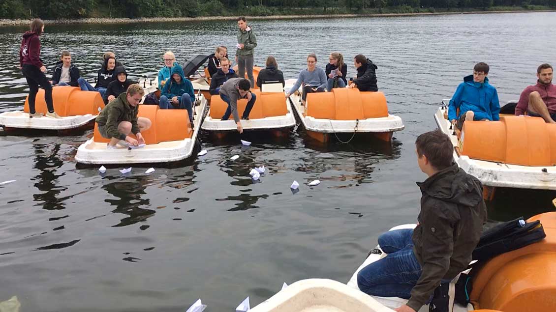 Jugendliche in Tretbooten auf dem Halterner Stausee lassen Papierschiffchen zu Wasser.